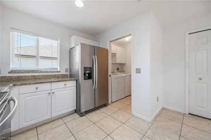 Kitchen with white cabinetry, stainless steel appliances, light stone counters, and light tile patterned floors