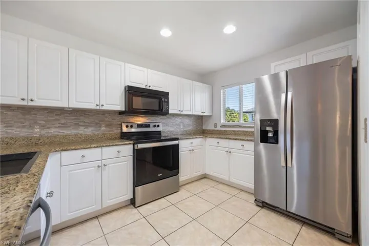 Kitchen featuring stainless steel appliances, white cabinetry, light stone countertops, and recessed lighting