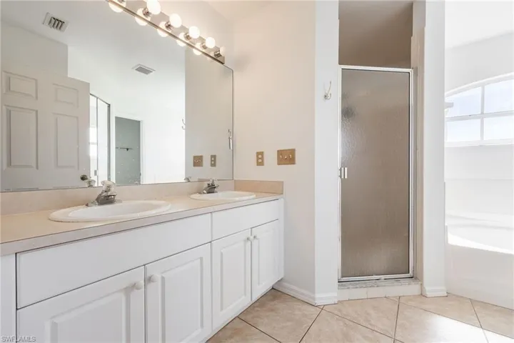 Full bathroom with a stall shower, double vanity, light tile patterned floors, and a garden tub