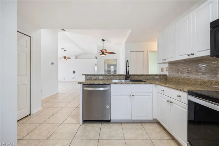 Kitchen with white cabinetry, a peninsula, black appliances, lofted ceiling, and dark stone counters