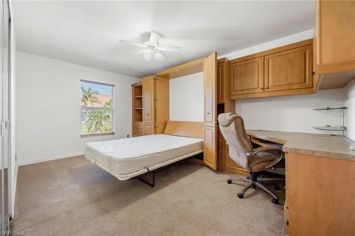 Bedroom with light colored carpet, ceiling fan, and an office area