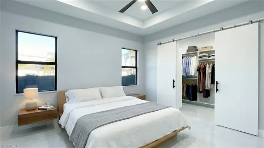 Bedroom featuring a raised ceiling, a barn door, a spacious closet, a ceiling fan, and recessed lighting