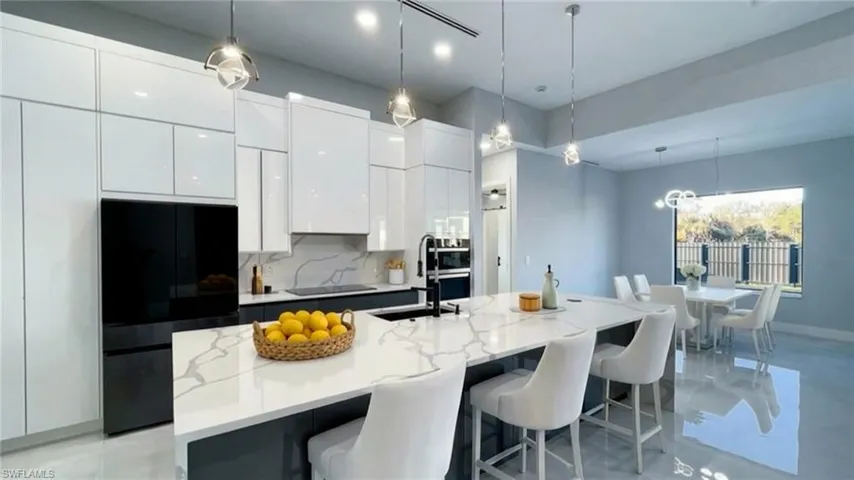 Kitchen featuring refrigerator, pendant lighting, modern cabinets, light stone counters, and a center island with sink
