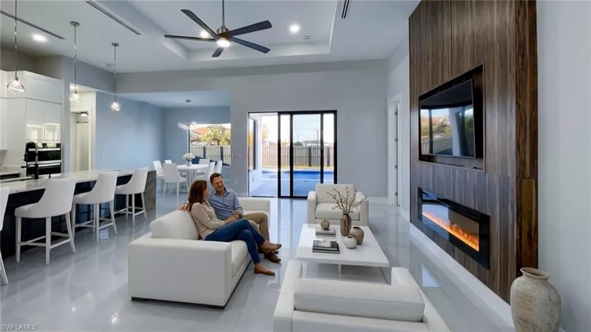 Living area with a glass covered fireplace, ceiling fan, a tray ceiling, and recessed lighting
