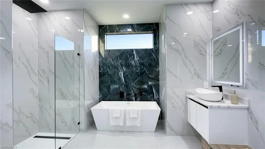 Bathroom with stone wall, vanity, a freestanding tub, a marble finish shower, and tile walls
