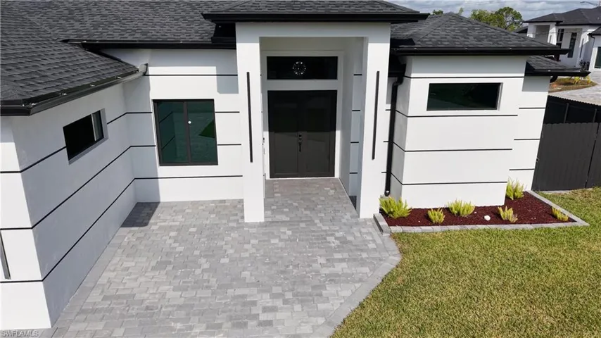 View of exterior entry featuring roof with shingles, a lawn, and stucco siding
