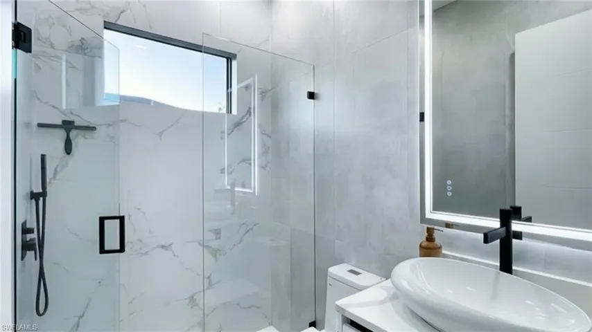 Bathroom with vanity, a marble finish shower, and tile walls