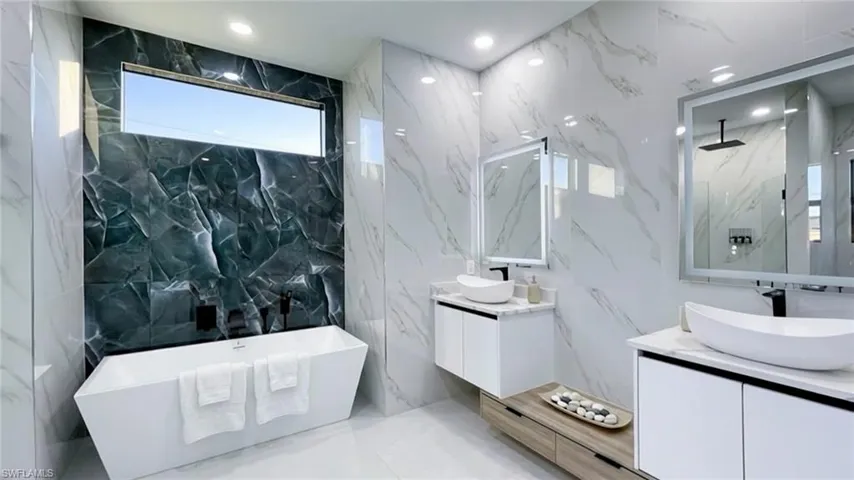 Full bath featuring stone wall, two vanities, a soaking tub, recessed lighting, and tile walls