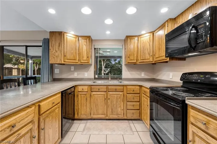 Kitchen with wood cabinetry, solid surface countertops & black appliances
