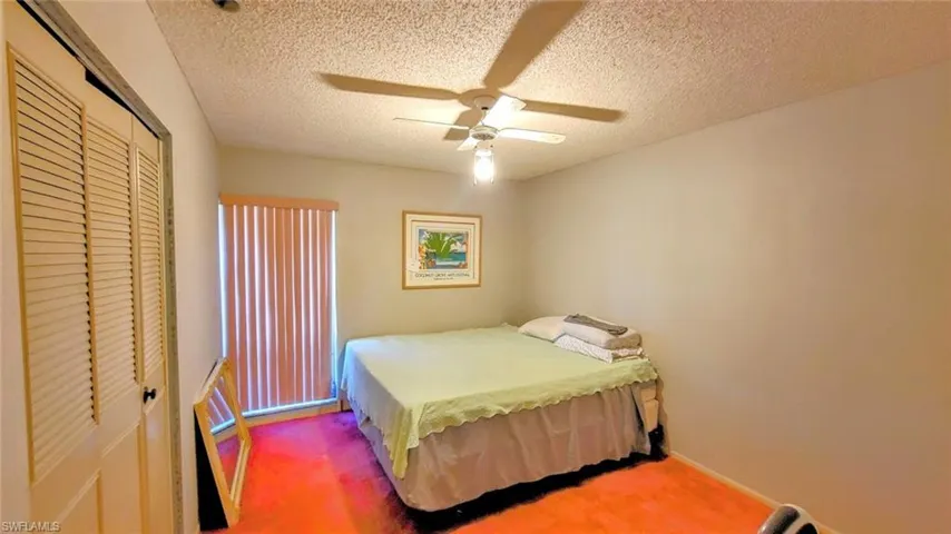 Carpeted bedroom with ceiling fan, a closet, and a textured ceiling