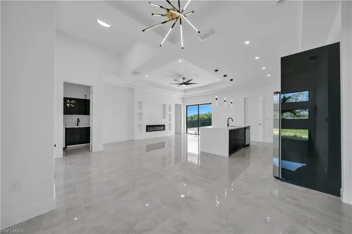 Unfurnished living room featuring a glass covered fireplace, light marble finish flooring, recessed lighting, a raised ceiling, and built in features
