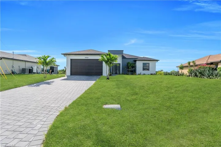 View of front of house featuring stucco siding, decorative driveway, a front lawn, and an attached garage