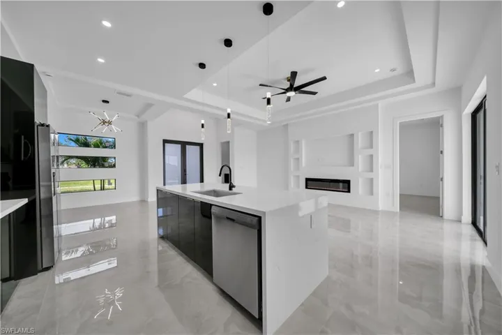 Kitchen featuring open floor plan, a glass covered fireplace, a raised ceiling, decorative light fixtures, and modern cabinets
