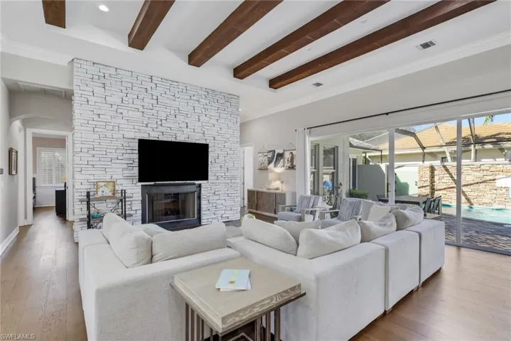 Living room featuring hardwood / wood-style floors, beamed ceiling, arched walkways, a sunroom, and a stone fireplace