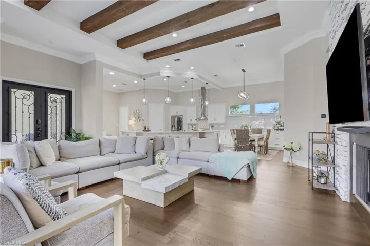 Living room with crown molding, wood finished floors, beam ceiling, french doors, and recessed lighting