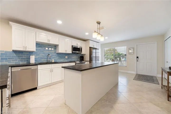 Kitchen featuring a center island, stainless steel appliances, pendant lighting, white cabinetry, and tasteful backsplash