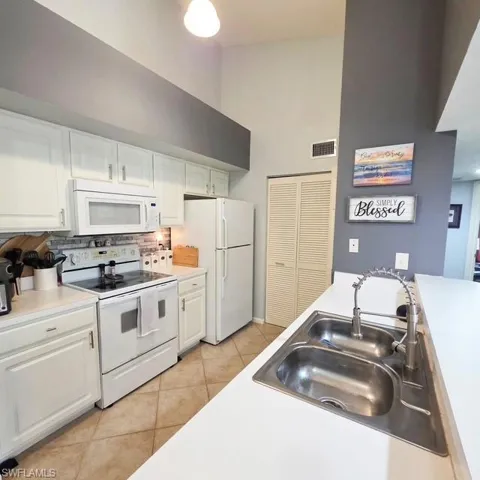 Kitchen featuring white cabinets, light countertops, white appliances, a high ceiling, and light tile patterned floors