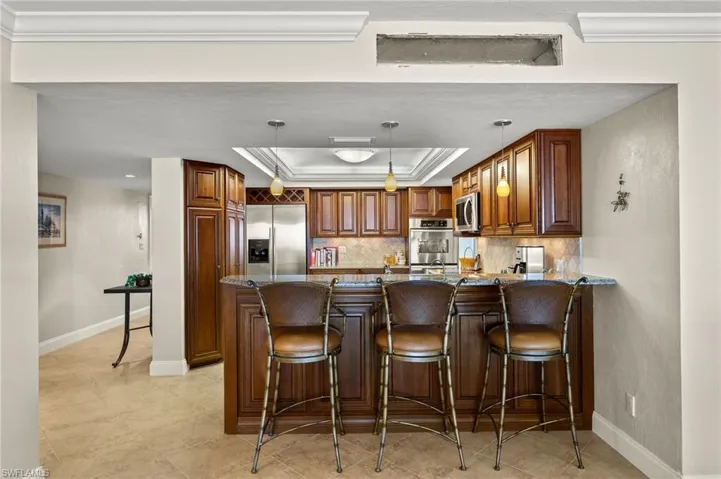 Kitchen with kitchen peninsula, hanging light fixtures, a raised ceiling, appliances with stainless steel finishes, and dark stone countertops