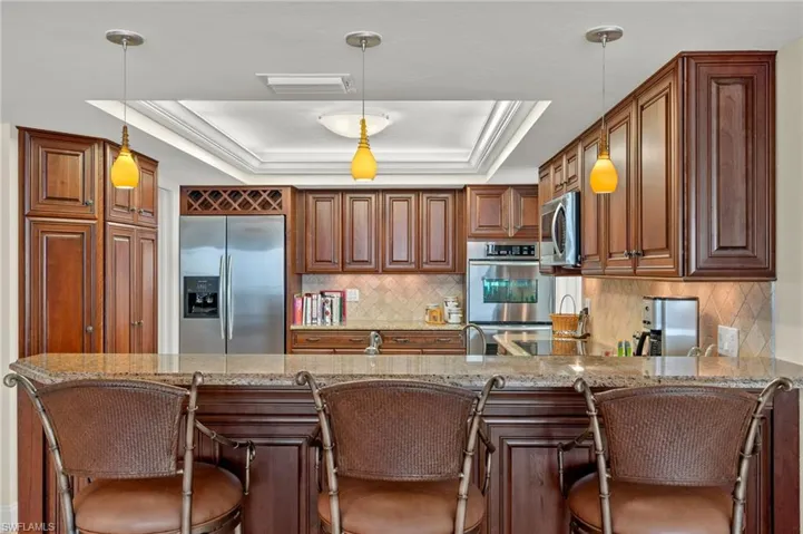 Kitchen with appliances with stainless steel finishes, hanging light fixtures, kitchen peninsula, and a tray ceiling