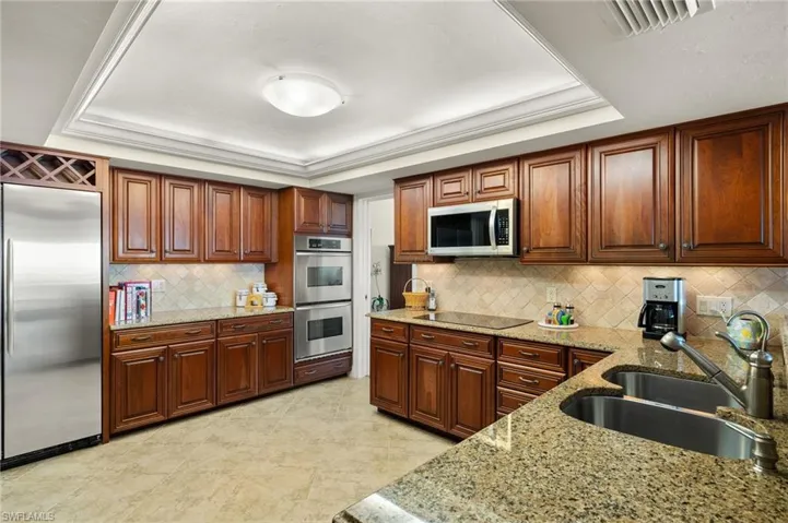 Kitchen with light stone counters, sink, tasteful backsplash, stainless steel appliances, and a tray ceiling