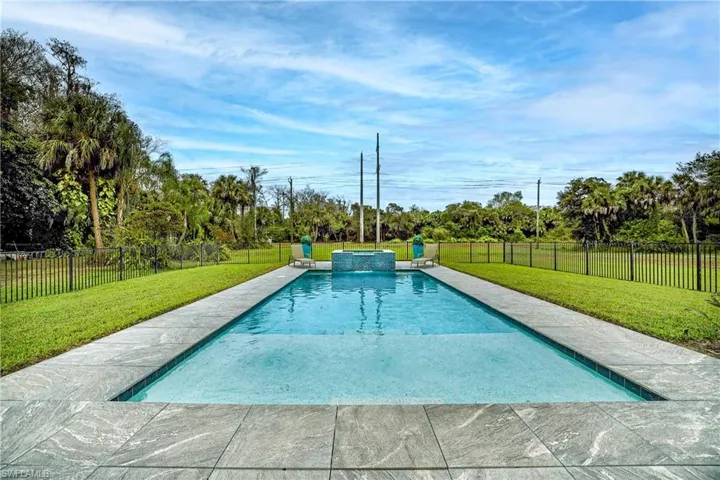 View of swimming pool with a fenced backyard, a patio area, a pool with connected hot tub, and view of scattered trees