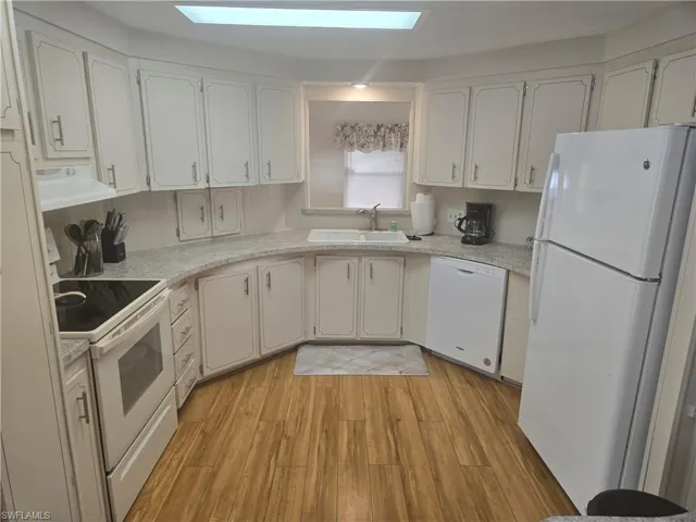 Kitchen featuring white appliances, sink, light wood-type flooring, range hood, and white cabinetry