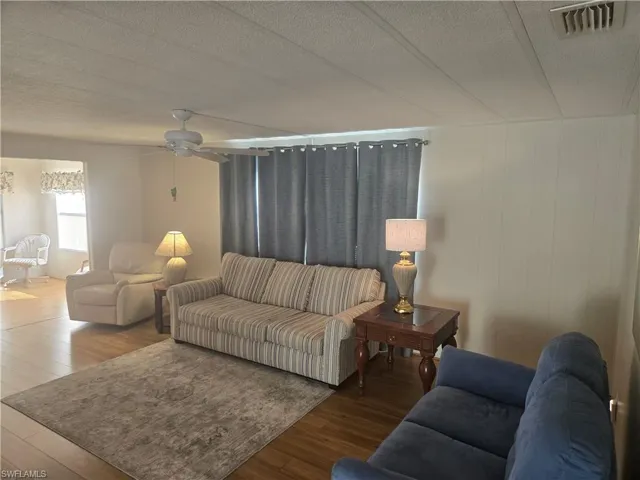 Living room featuring ceiling fan, wood-type flooring, a textured ceiling, and wooden walls