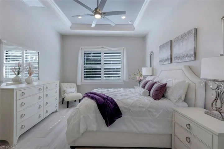 Bedroom with ceiling fan, a tray ceiling, and light hardwood / wood-style floors