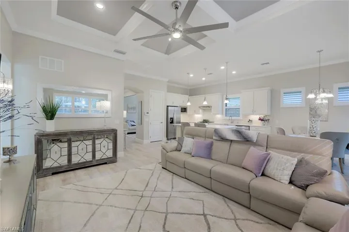 Living room with light hardwood / wood-style flooring, crown molding, beamed ceiling, ceiling fan with notable chandelier, and coffered ceiling