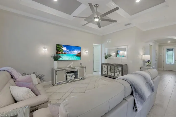 Living room featuring ornamental molding, light wood-type flooring, beamed ceiling, coffered ceiling, and ceiling fan