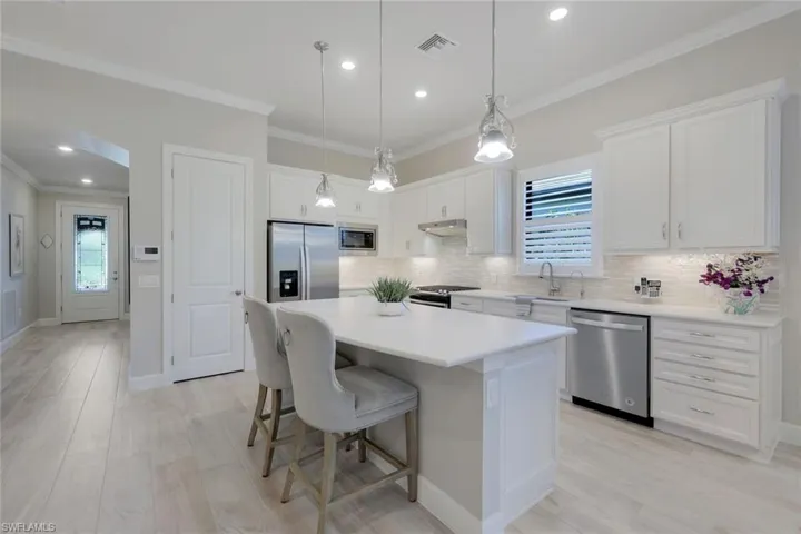 Kitchen with decorative light fixtures, a kitchen island, backsplash, ornamental molding, and appliances with stainless steel finishes