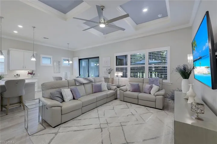 Living room featuring coffered ceiling, ceiling fan, ornamental molding, and light wood-type flooring