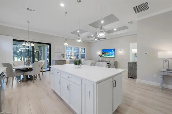 Kitchen with coffered ceiling, a center island, white cabinetry, light wood-type flooring, and pendant lighting