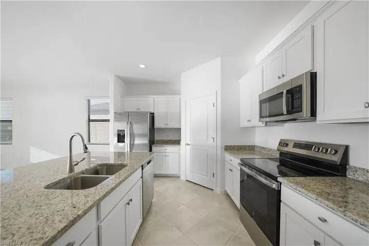 Kitchen featuring appliances with stainless steel finishes, white cabinetry, light stone counters, recessed lighting, and light tile patterned floors
