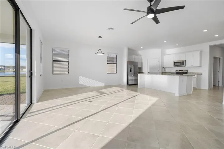 Kitchen featuring open floor plan, stainless steel appliances, a ceiling fan, light tile patterned floors, and a center island with sink