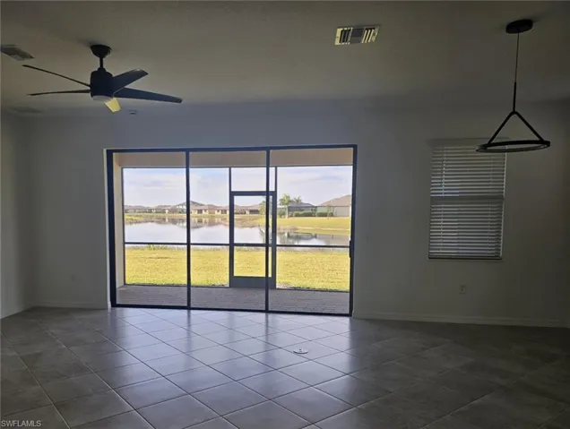Unfurnished room featuring a ceiling fan, dark tile patterned floors, and a water view