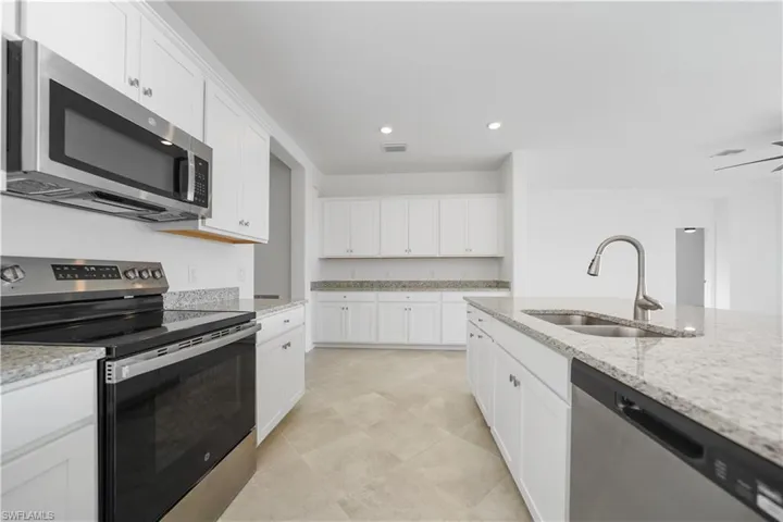 Kitchen with appliances with stainless steel finishes, white cabinetry, recessed lighting, and light stone counters