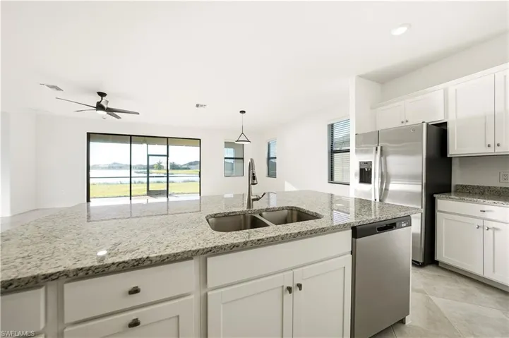 Kitchen with white cabinets, stainless steel appliances, light stone counters, ceiling fan, and healthy amount of natural light