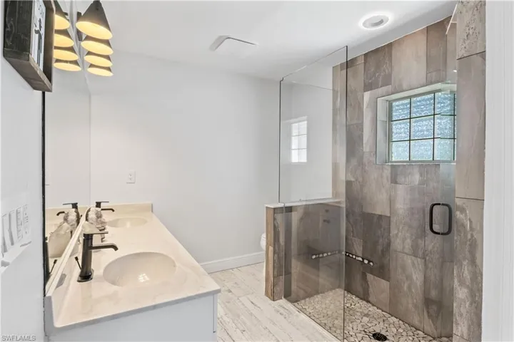 Full bath with plenty of natural light, double vanity, a stall shower, and wood finished floors