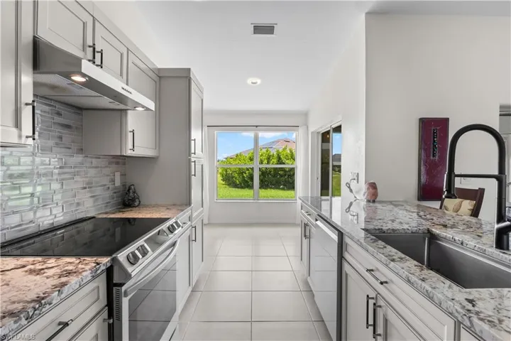 Kitchen featuring appliances with stainless steel finishes, under cabinet range hood, decorative backsplash, light tile patterned flooring, and light stone counters