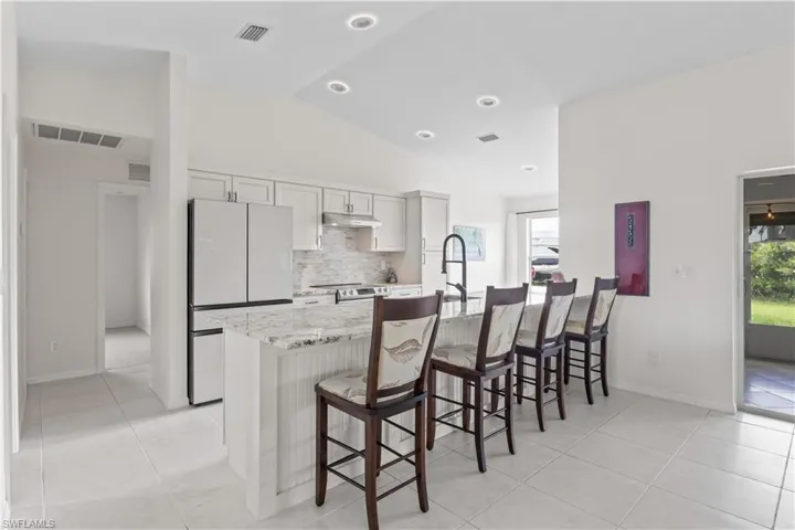Kitchen with freestanding refrigerator, under cabinet range hood, backsplash, vaulted ceiling, and a breakfast bar