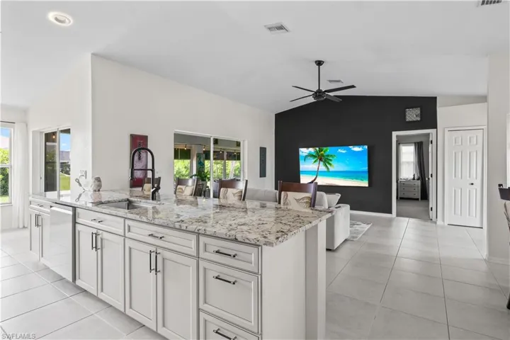 Kitchen with dishwasher, vaulted ceiling, light stone countertops, ceiling fan, and white cabinetry