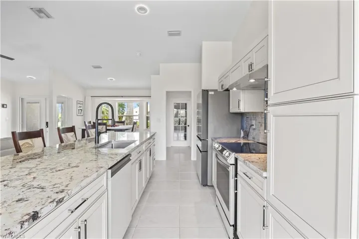 Kitchen featuring stainless steel appliances, under cabinet range hood, light stone counters, light tile patterned flooring, and decorative backsplash