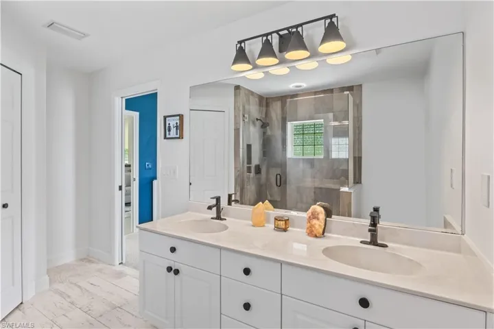 Full bathroom featuring double vanity, a shower stall, and marble look tile flooring