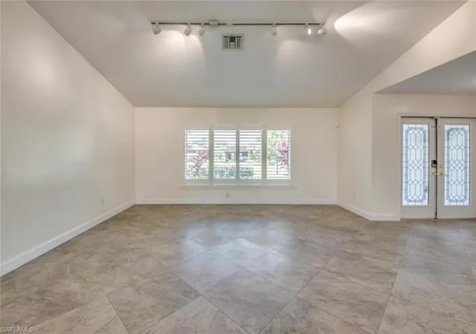 Spare room featuring lofted ceiling, rail lighting, french doors, and light tile patterned flooring