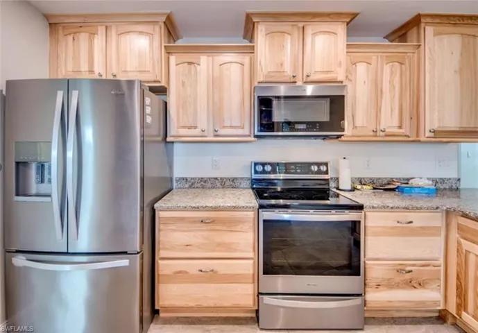 Kitchen with appliances with stainless steel finishes, light brown cabinets, and light stone countertops