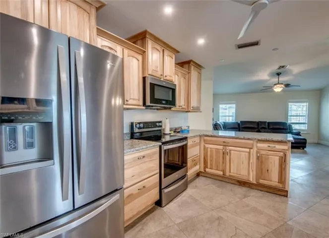 Kitchen with appliances with stainless steel finishes, light tile patterned floors, kitchen peninsula, light brown cabinetry, and ceiling fan