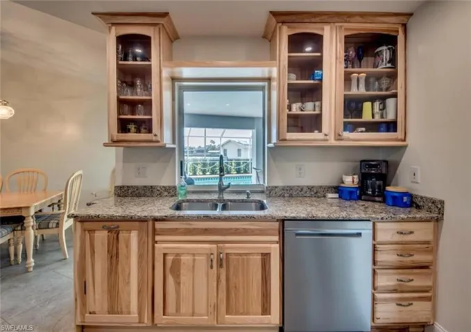 Kitchen with sink, stainless steel dishwasher, light tile patterned floors, and light stone countertops