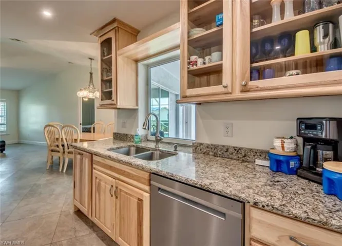 Kitchen with dishwasher, sink, light stone countertops, pendant lighting, and light brown cabinetry