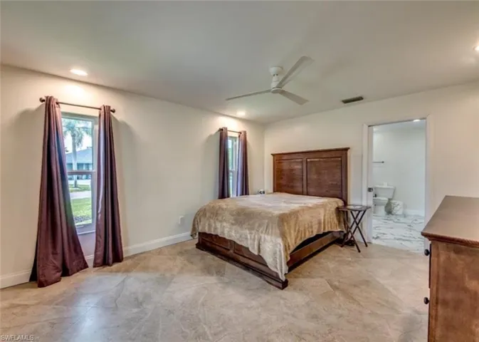 Bedroom with ceiling fan, light tile patterned flooring, and ensuite bath